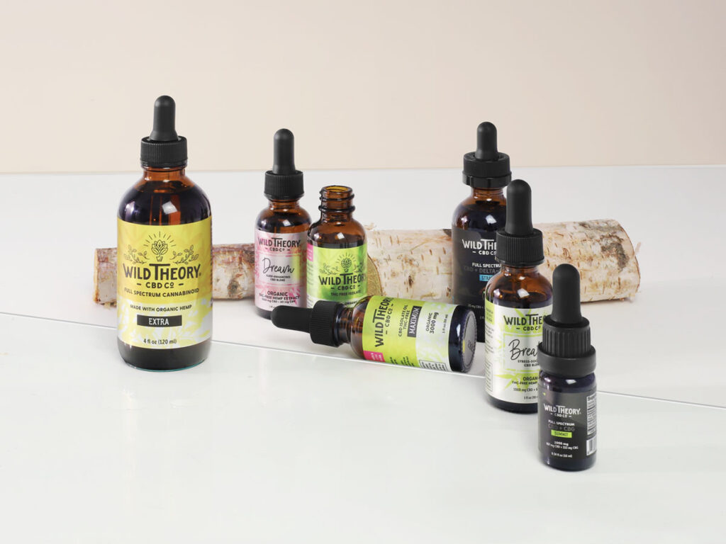 A collection of Wild Theory CBD Co. oil tinctures in various sizes displayed on a light surface, suggesting a range of hemp-derived wellness products offered by the brand.