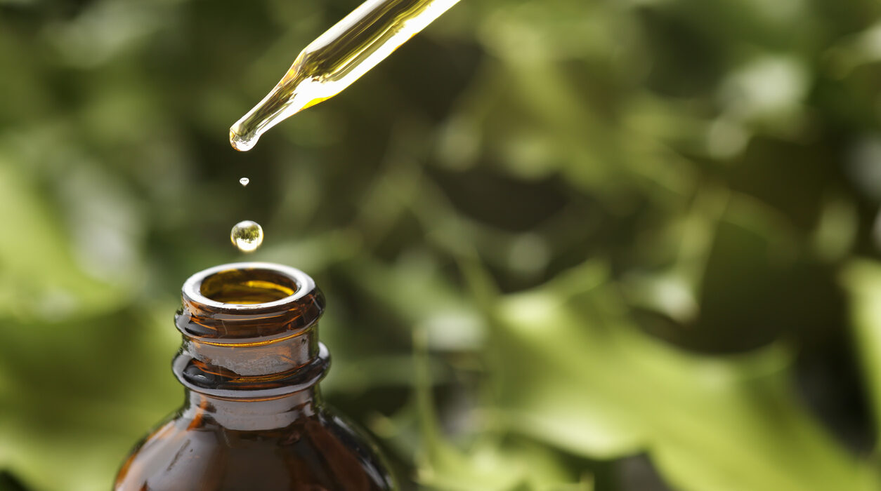 Drops of CBD OIl Falling Into a Brown Bottle from a Dropper With Green Background