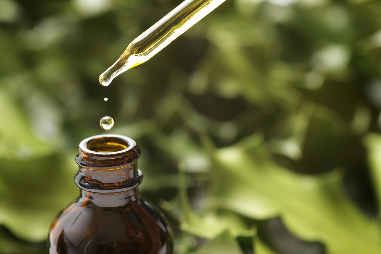 Drops of CBD OIl Falling Into a Brown Bottle from a Dropper With Green Background